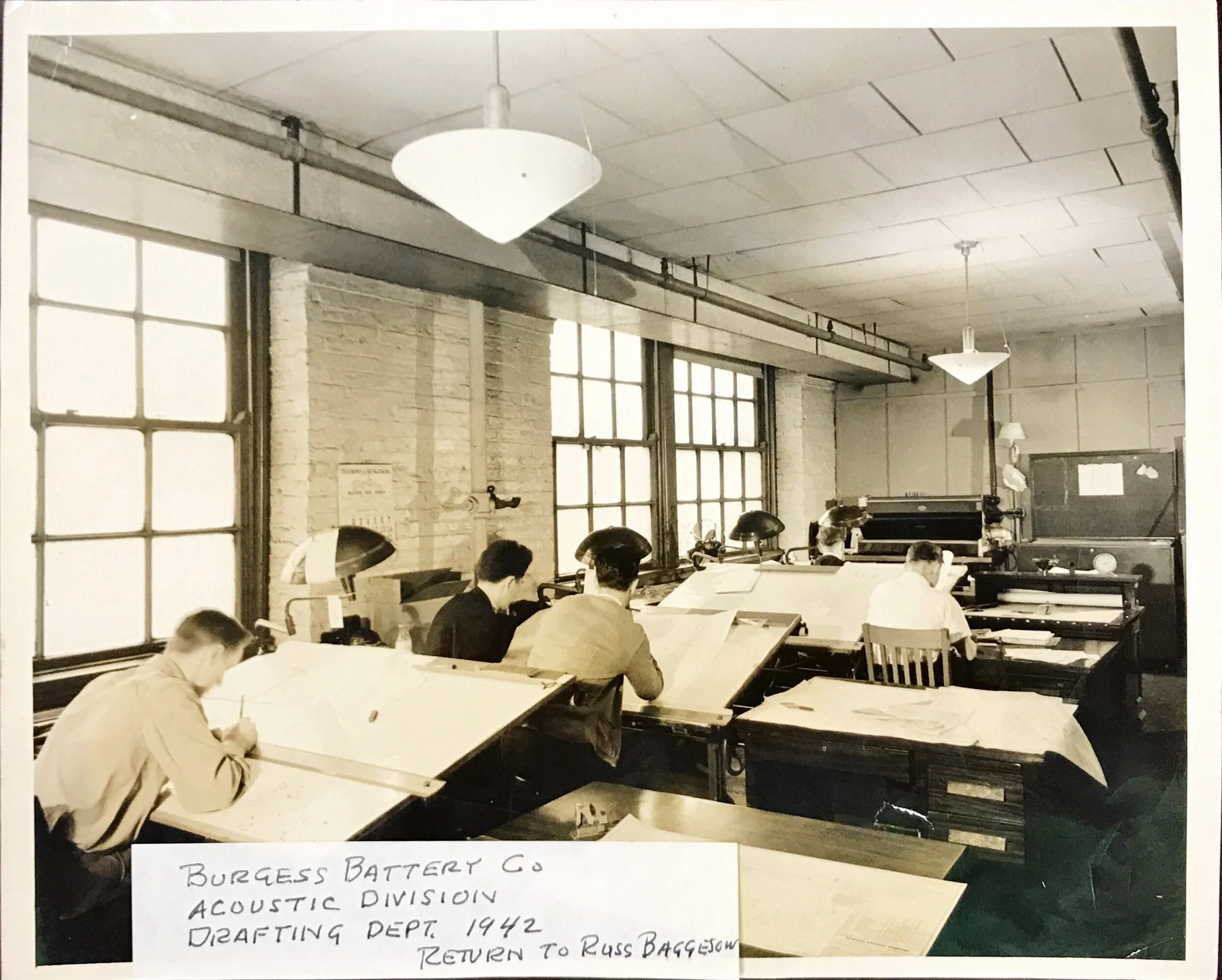 Historical image of the Burgess Battery Co Acoustic Division Drafting Department where men sit at drafting desks, drawing engineering designs for silencer in the 1940s.