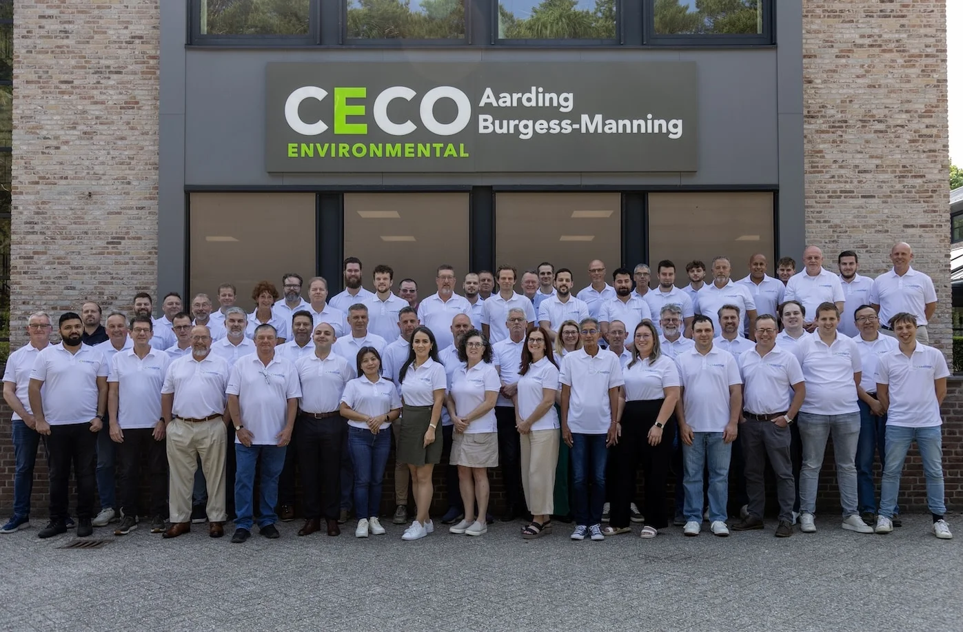 Burgess-Manning employees outside in front of building with a CECO Environmental Aarding Burgess-Manning sign, all wearing company shirts, smiling for the camera.
