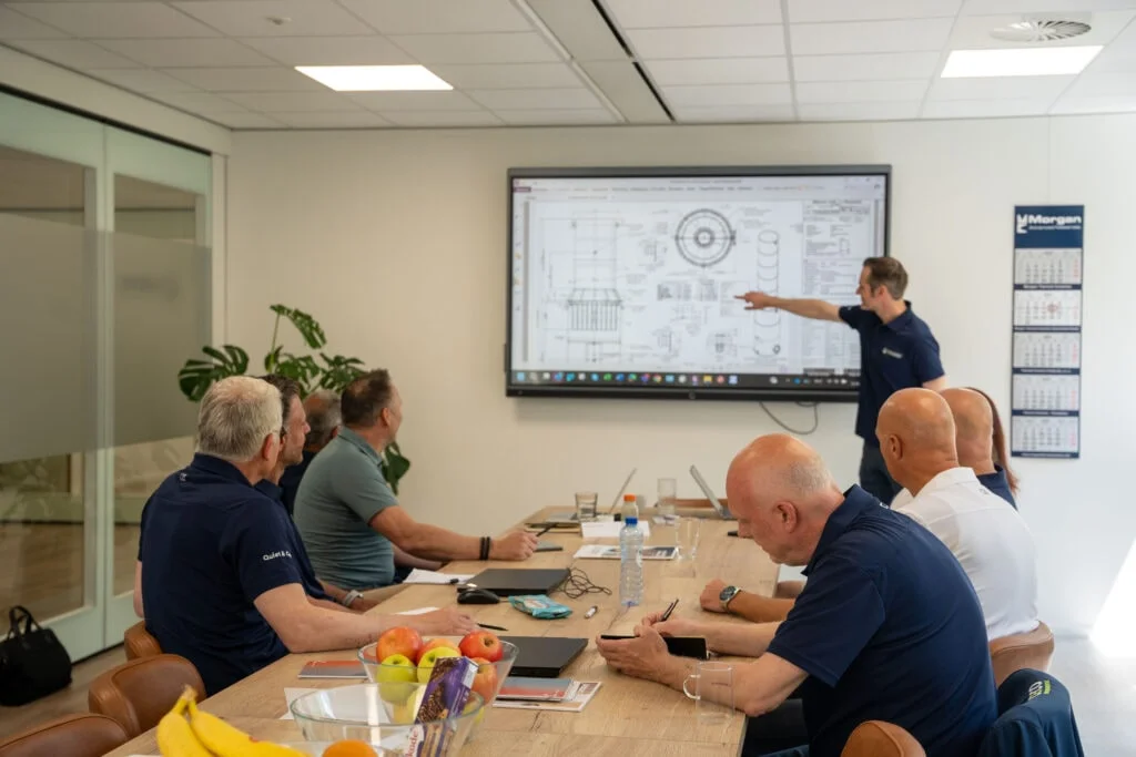Burgess-Manning employees in meeting discussing the engineering of industrial noise control silencers, showing a specification drawing of the customized noise reduction technology.
