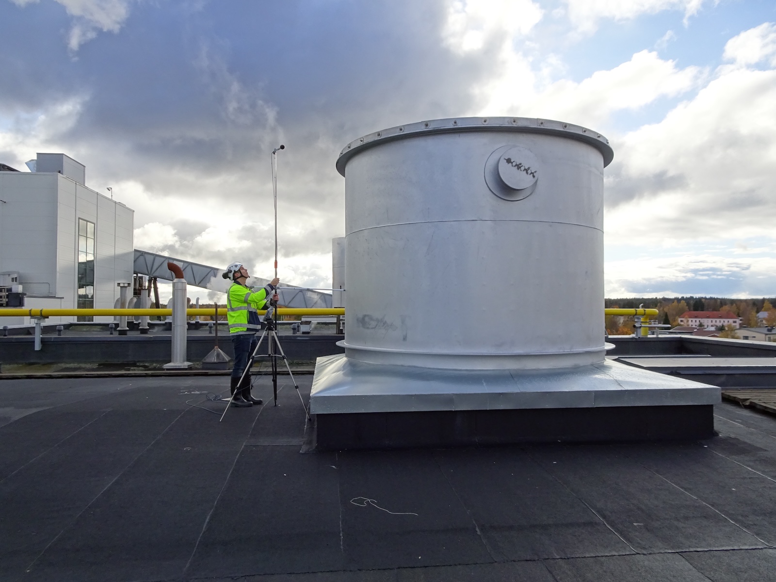 Burgess Manning worker on a rooftop using a sound level meter on a tripod, conducting a noise measurement survey for acoustical consultancy.
