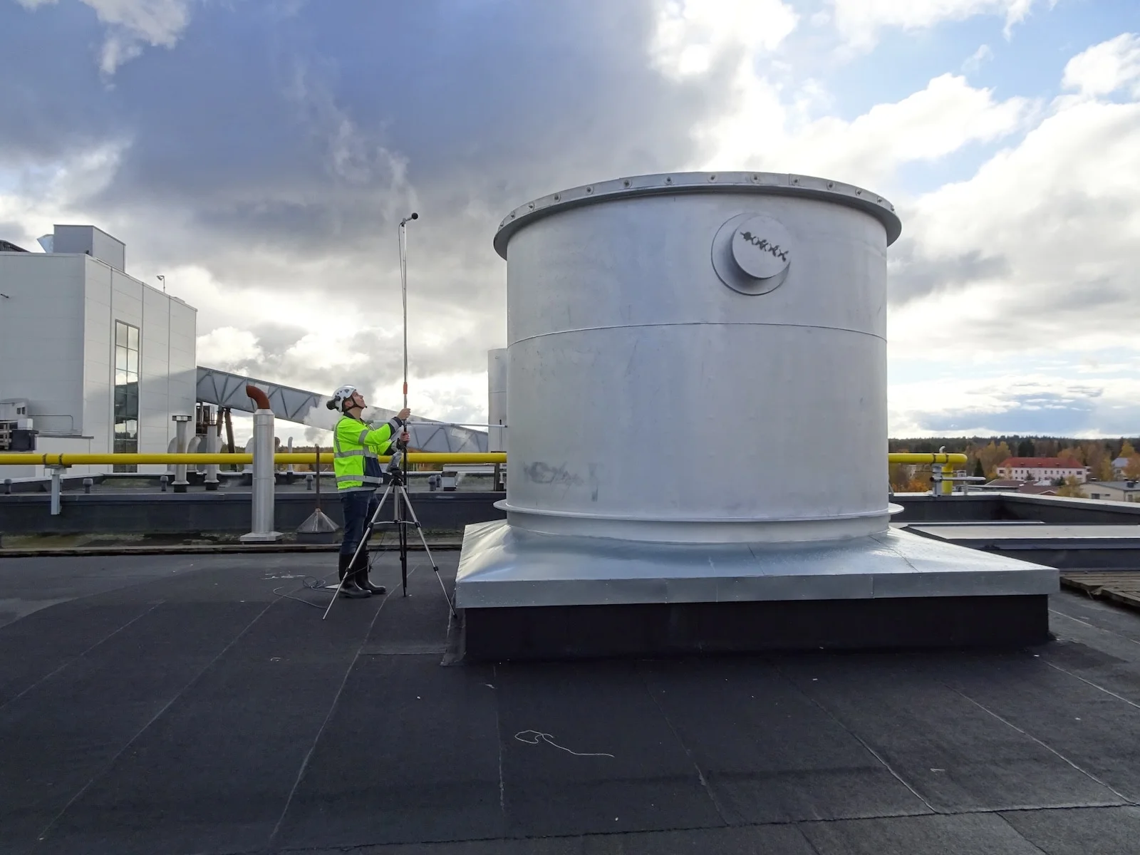 Burgess Manning worker on a rooftop using a sound level meter on a tripod, conducting a noise measurement survey for acoustical consultancy.